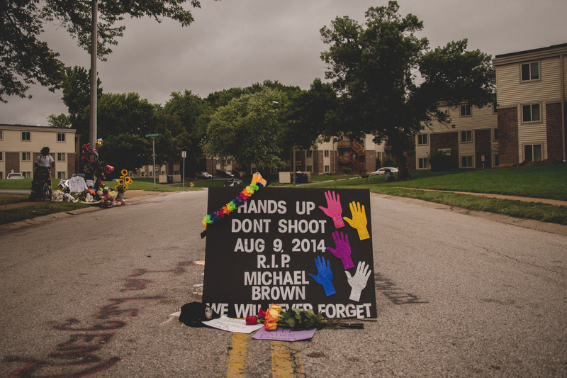 Memorial for Michael Brown Jr. on Canfield Drive reads "Hands Up Don't Shoot. August 9, 2014. RIP Michael Brown. We will never forget." 